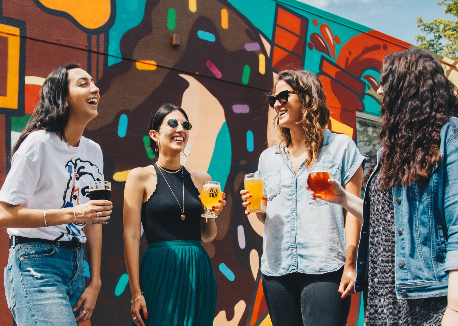 four women holding drinks while laughing together during daytime