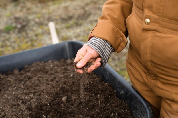 person in yellow jacket holding black soil